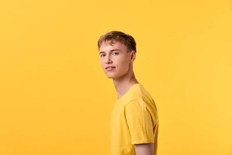 Young man in a yellow t shirt against a vivid yellow backdrop, showcasing casual fashion, relaxed pose, and confident demeanor suitable for lifestyle or product campaigns.