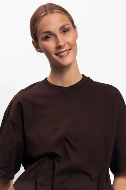Smiling young woman with light brown hair wears dark casual t shirt, posing against white background. Portrait of happy female model with natural makeup and relaxed confident expression.