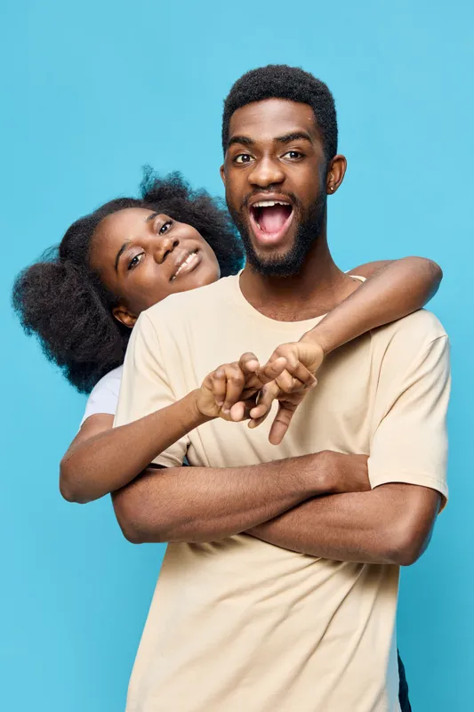 Happy young couple embracing against a bright blue background, showcasing love and joy with playful expressions Vibrant colors highlight their energy