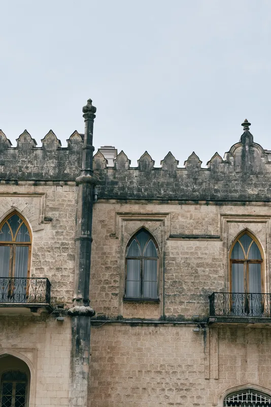 Architectural historic stone castle building with arched windows and battlements, capturing a timeless facade against a pale sky, inviting exploration and imagination and presenting a calm historic