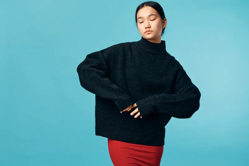 Woman in black sweater and red skirt posing with closed eyes against blue background for fashion, elegance, style and casual clothing portrait in studio with calm expression.