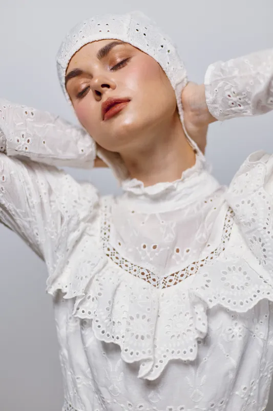 Young model in elegant white lace outfit showcases a serene expression against a light background, highlighting contemporary fashion and individuality