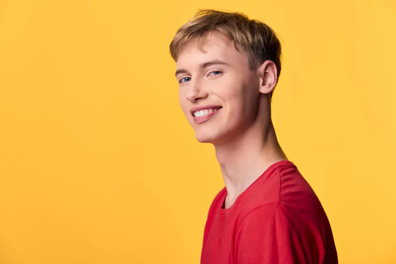 Smiling young man in a red shirt against a bright yellow background, energetic and friendly, studio lighting with clean tones, casual expression suitable for lifestyle, youth, or promotional content.