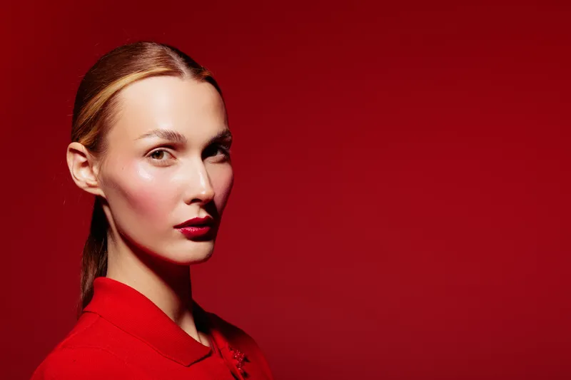 Portrait of a young woman with red lipstick and red clothing against a red background. Concept of fashion, beauty, and confident female model with stylish makeup.