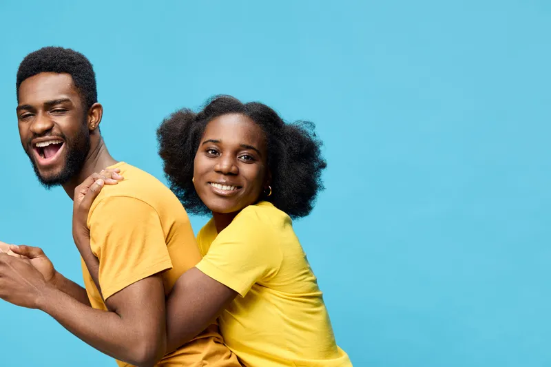 Joyful young African couple in matching yellow t shirts on a bright blue background, expressing happiness and togetherness
