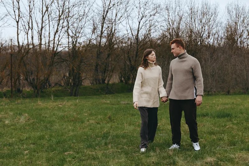 A couple walks hand in hand in a grassy park, wearing cozy sweaters, enjoying a calm outdoors moment in autumn landscape, warm mood and simple lifestyle.
