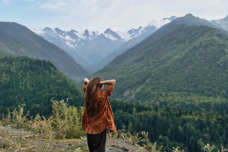 Woman standing with hands behind head on rocky overlook, mountains valley nature hiking landscape scene with authenticity inclusivity, solitude and exploration outdoors
