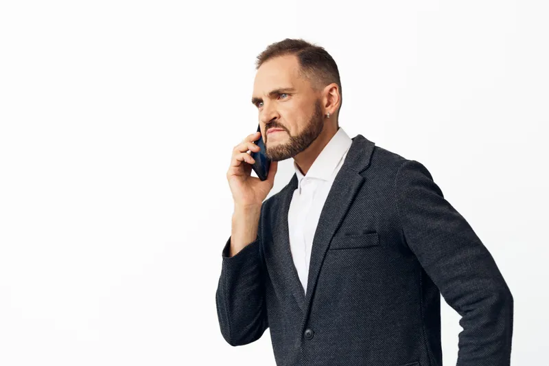 A professional business man speaks on a mobile phone, standing against an isolated colored background, showcasing calm confidence, focus, and leadership in a modern setting.