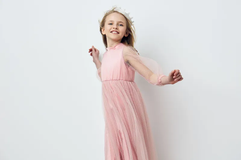 Joyful girl in a pink dress with flower crown dancing against a minimalist white background, embodying happiness and innocence, perfect for children s fashion themes