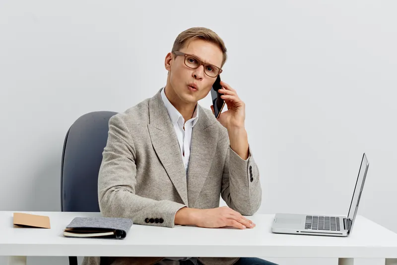 focused man talking smartphone laptop digital nomad remote work business casual glasses in office white background