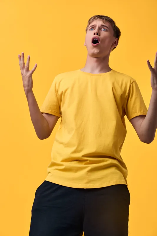 Man in yellow shirt shows astonishment against a vivid studio background, arms raised and expression surprised, capturing emotion and dynamic gesture for energetic campaigns