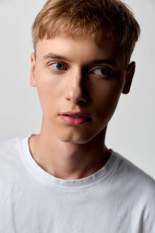 Close up of a young man in a white tee with a calm thoughtful expression, soft lighting and smooth skin for fashion, beauty and lifestyle projects