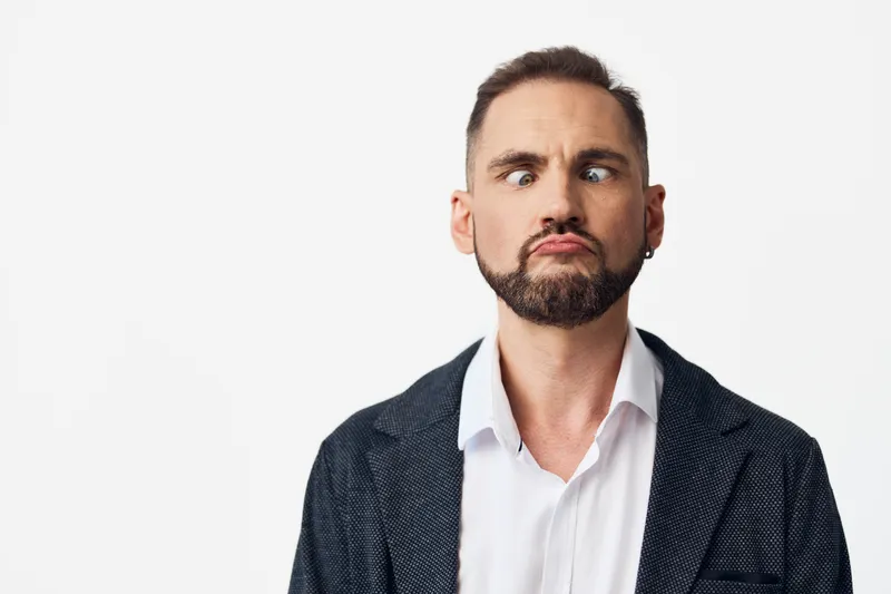 A professional business man stands against an isolated colored background, showing a curious and puzzled expression, conveying doubt and focus in a corporate portrait.