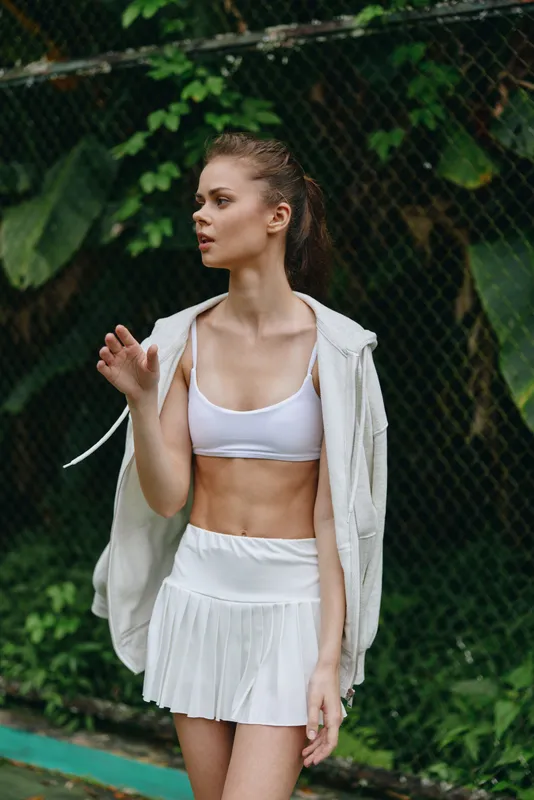 Young athletic woman in sporty outfit with a cropped top and skirt, enjoying outdoor workout against a lush green backdrop