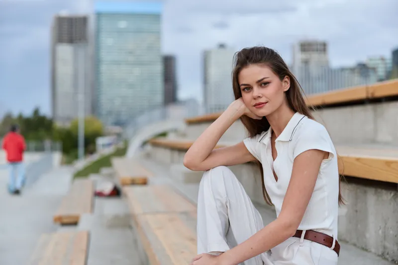 Business woman in a modern urban setting, showcasing confidence and style with a neutral outfit, sitting on a bench amidst a lively cityscape.