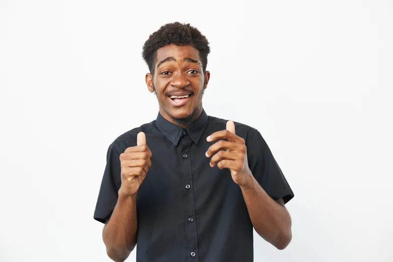 Happy African American man expressing excitement and joy with a cheerful smile against a clean white background, showcasing a casual outfit and positive energy.