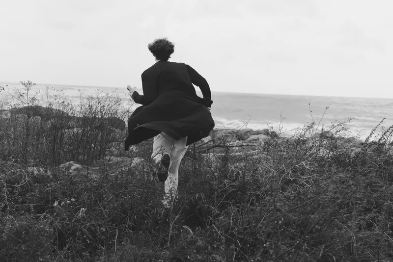 Silhouette of a woman leaping along a windy coast, captured in monochrome, conveying freedom, motion, and rugged shoreline with dramatic outdoor atmosphere.