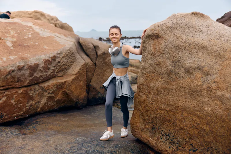 Young athletic woman in sportswear joyfully walking between rocks by the sea, expressing health and fitness lifestyle