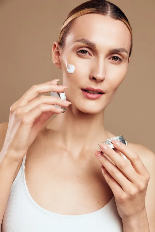 Woman applying face cream with hands, close up portrait on beige background, skincare and self care concept, spa beauty routine, soft studio lighting, calm wellness mood