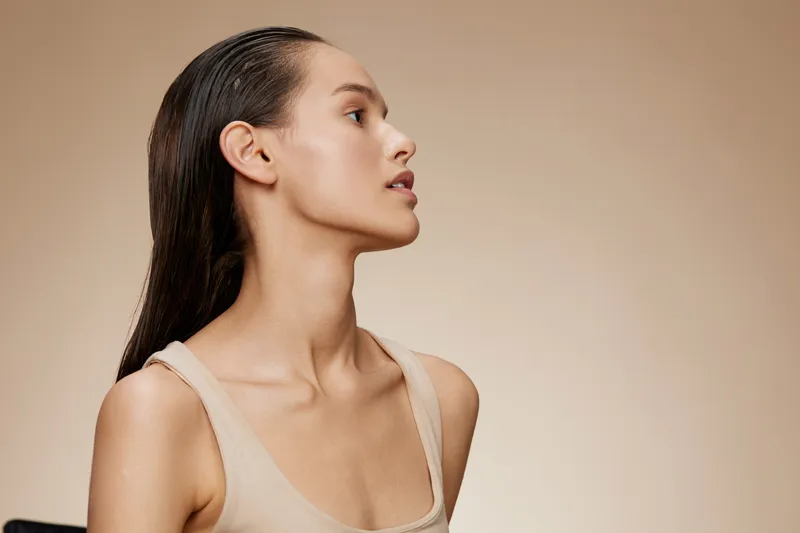 Elegantly poised model showcasing radiant skin, natural makeup, and subtle elegance against a soft beige background Beauty, confidence, and minimalism define this artful composition