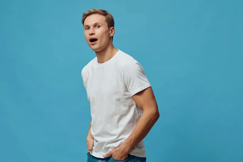 surprised young caucasian man in casual white t-shirt standing blue background amazed expression digital detox concept lifestyle portrait