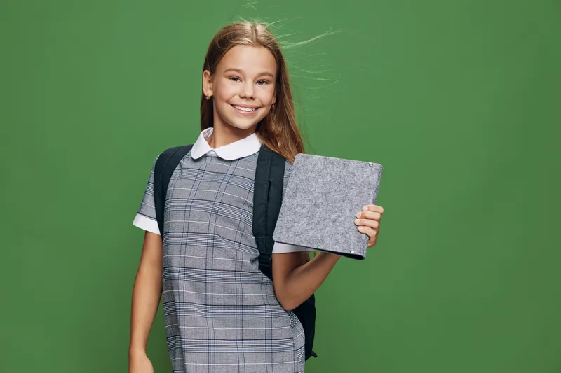 Girl student smiling and holding digital tablet with backpack on green background for education, technology and back to school concept in studio portrait