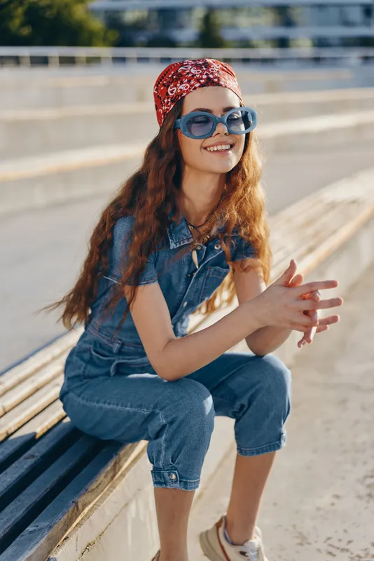 lifestyle woman in modern boho-western denim street style wearing sunglasses and red bandana, smiling outdoors with warm film color tones and casual summer vibe