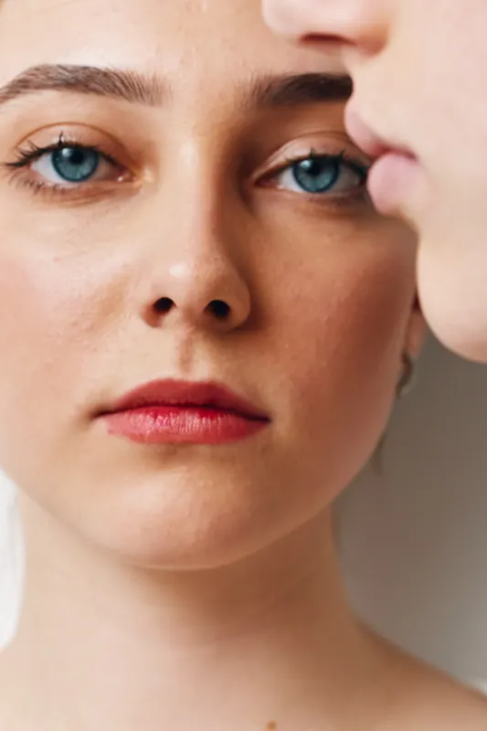 Closeup portrait of woman with blue eyes and natural skin looking at camera. Female face with red lips and light makeup in bright soft lighting for beauty and skincare.