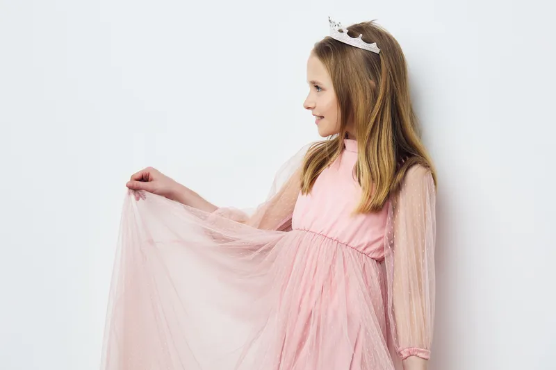 Happy girl in a pink dress with a crown, showcasing joy in a bright, minimalistic background, perfect for children s fashion and celebrations