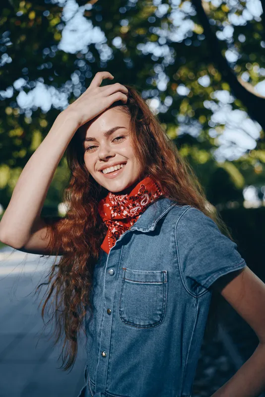 Lifestyle woman in modern boho-western denim street style with a red bandana smiling outdoors in film color under natural sunlight.