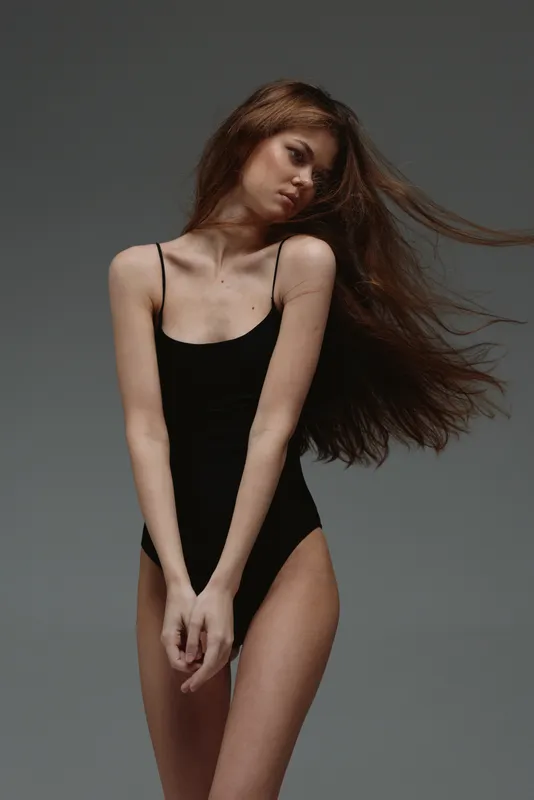 slender woman posing in black bodysuit with flowing hair against dark background, graceful and elegant mood