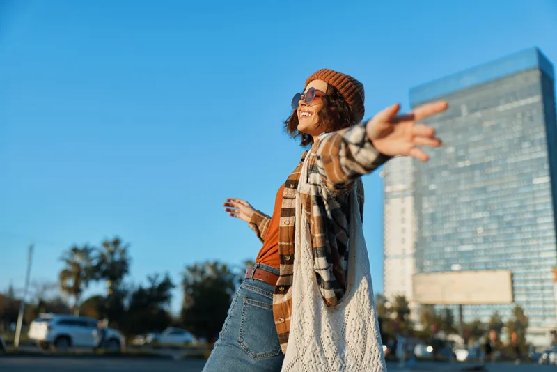 Woman smile urban city joyful arms sunlight portrait of a carefree young traveler in boho hat and sunglasses, authenticity and candid lifestyle with golden hour glow and mindful living vibes.