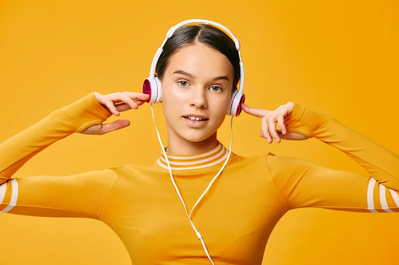Active woman in a bright orange top wearing headphones in a studio, showcasing fitness, sport energy and music inspiration for a dynamic workout concept.