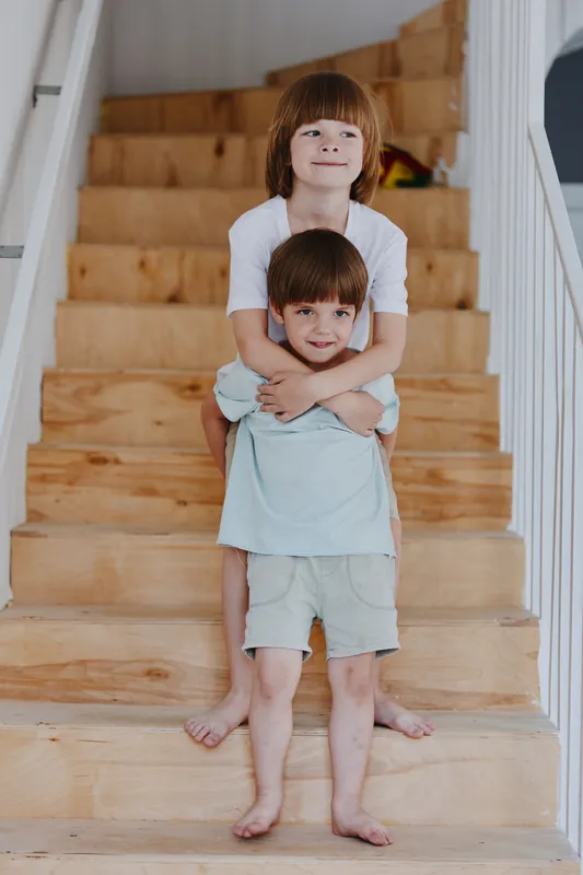 Two cheerful boys playfully posing on a staircase, showcasing a sense of joy and sibling bond. Their casual attire adds to the warm atmosphere of the moment.