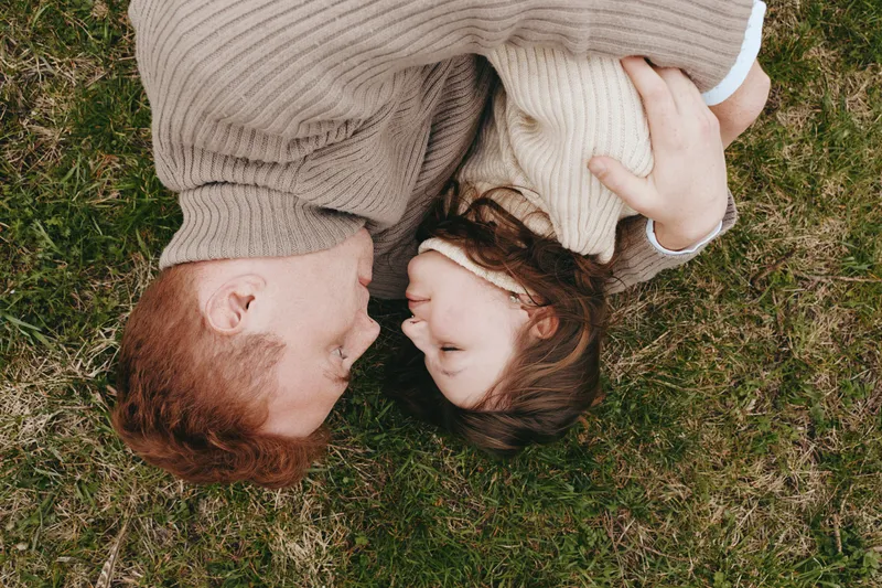 A family rests on grass with a playful goat kid nearby, capturing a warm, relaxed moment. Casual lifestyle scene showing affection, harmony, and gentle outdoors living, emphasizing everyday bond and