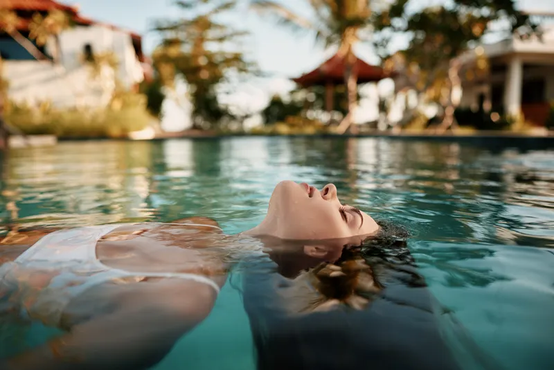 Pool relaxation for a woman floating on her back, water around her, sunshine warming the skin. A tranquil scene conveys leisure, vacation mood, and a peaceful summer resort vibe.