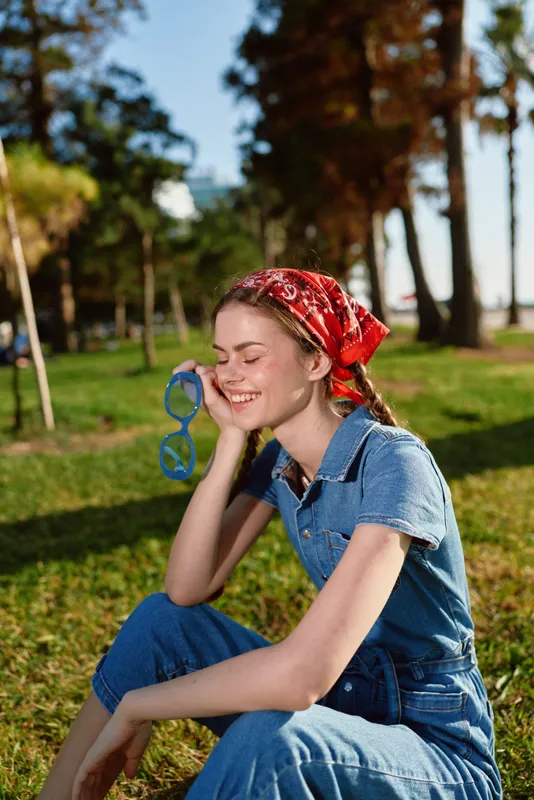 lifestyle woman in modern boho-western denim street style smiling outdoors with red bandana and blue sunglasses, film color natural light relaxation