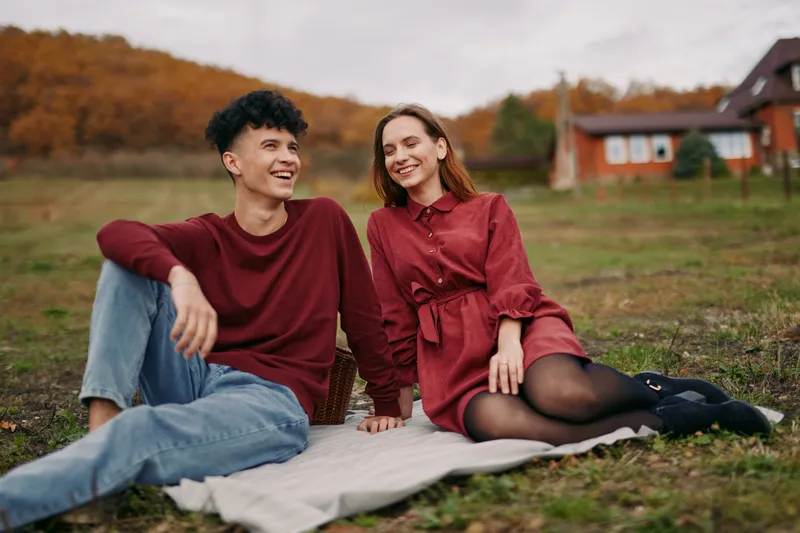 An authentic, candid moment with two friends relaxing on a blanket in a sunlit autumn field, showcasing natural expressions and genuine connection.