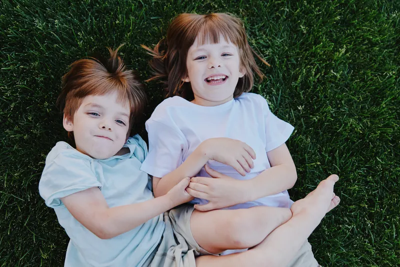 Playful children enjoying a sunny day outdoors, lying on the grass, sharing smiles and laughter in a vibrant, cheerful atmosphere.