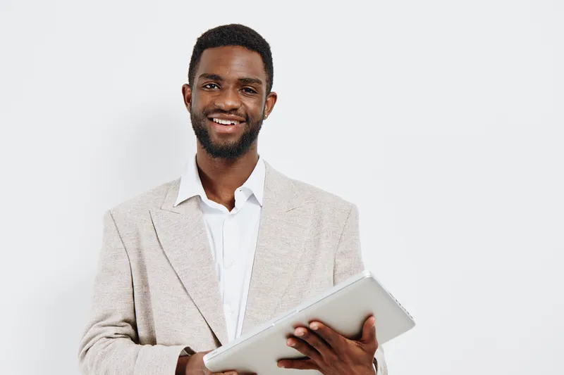 Professional smiling man holding tablet in hand, dressed in beige blazer and white shirt, isolated on plain white background. Business, technology, education, corporate, casual, confident, modern, adu