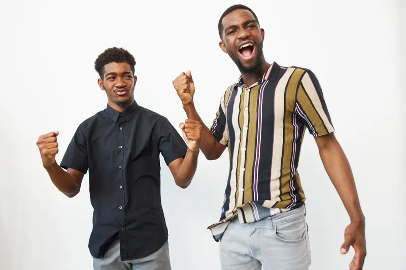 Two joyful African American men expressing excitement and victory with their fists raised, showcasing a celebratory mood and vibrant energy.
