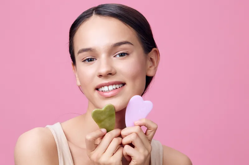 Beautiful woman showcasing jade and rose quartz gua sha tools, promoting skincare and self care, emphasizing relaxation and wellness for a glowing complexion