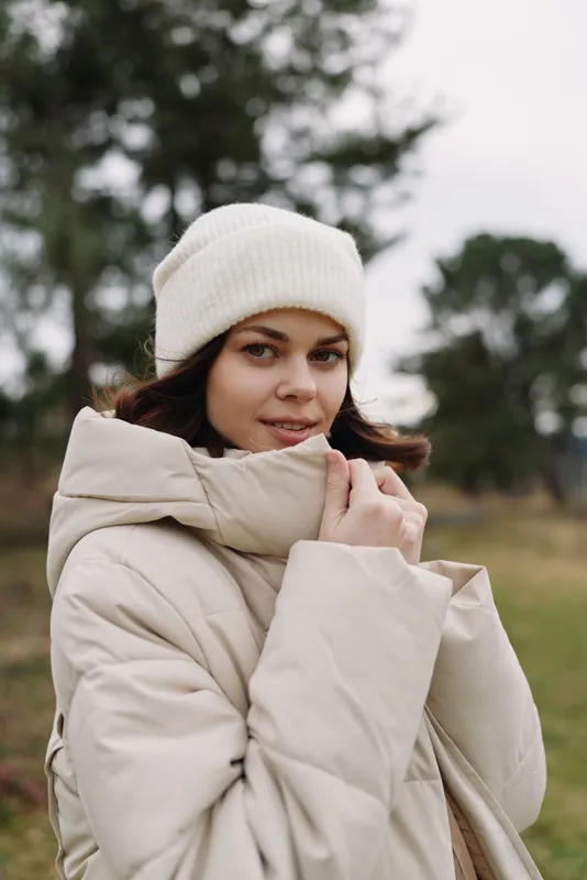 woman wearing a coat and beanie in an outdoor winter setting, showcasing fashion and cozy outerwear with a calm natural ambience, relaxed portrait mood, gentle light highlighting textures