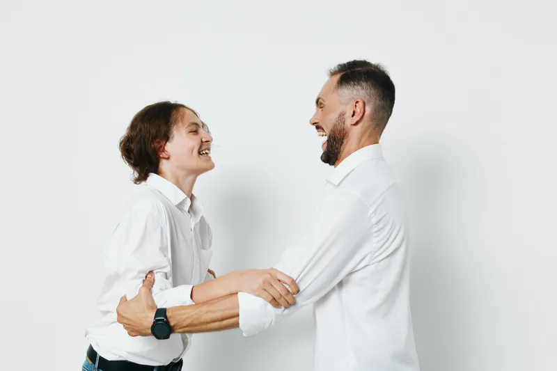 A professional man in business attire shares a joyful moment with a colleague on a clean isolated white background, signaling approachable leadership and confident teamwork.