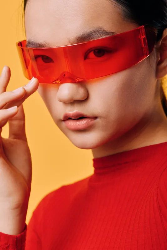 Woman portrait with red sunglasses and red turtleneck sweater on orange background. Closeup of female face with smooth skin and modern fashion style in studio lighting.