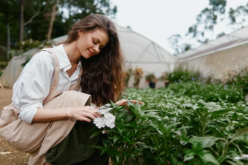 Beautiful young woman enjoying gardening in a greenhouse, surrounded by blooming flowers nurturing plants evokes emotions of joy and serenity
