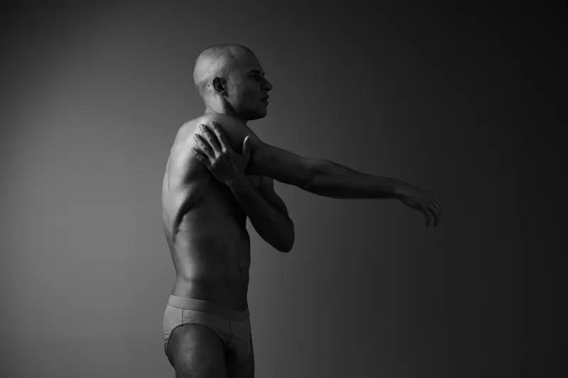 Black and white image of a man stretching his arms, showcasing a sense of personal care and well-being, highlighting physical fitness and relaxation.