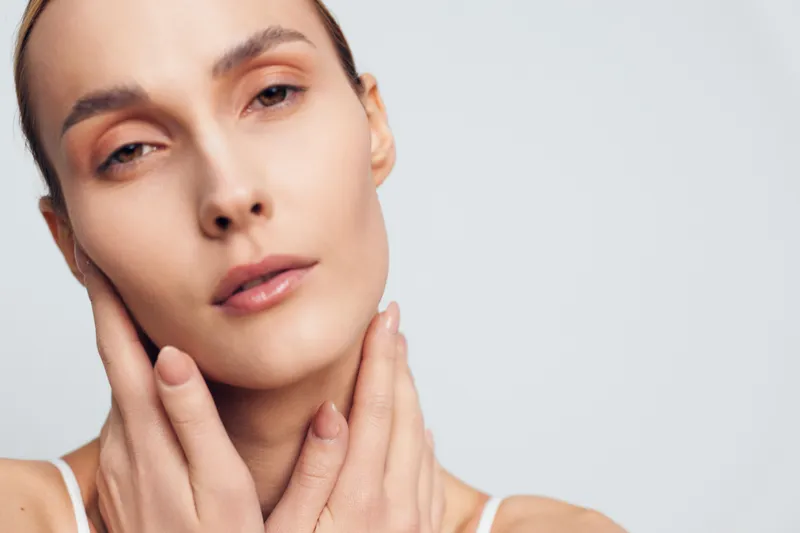 Woman skincare face portrait closeup cream hands cheeks, calm expression, smooth skin on light studio background, beauty wellness concept, soft studio lighting