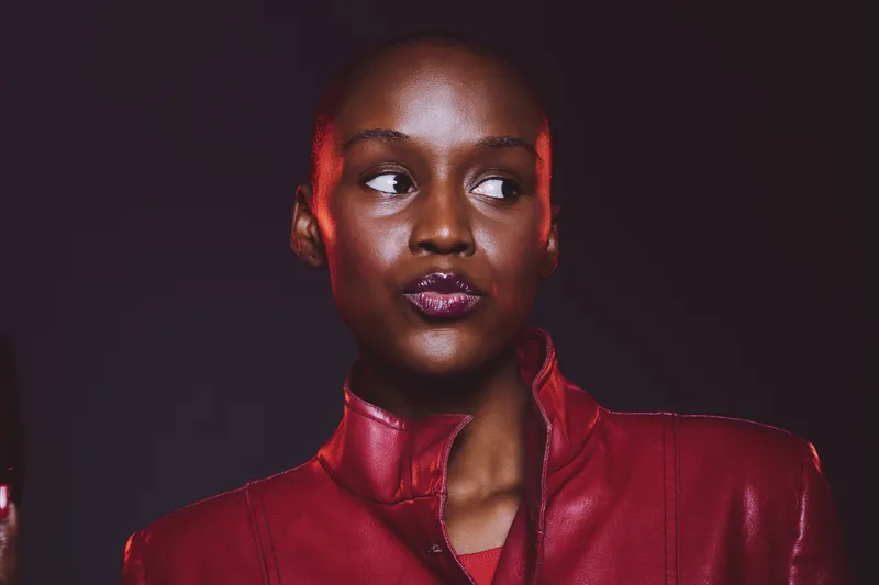 Portrait of confident dark skinned African woman wearing red leather jacket looking sideways. Studio shot with dramatic lighting on black background. Concept of fashion and beauty.