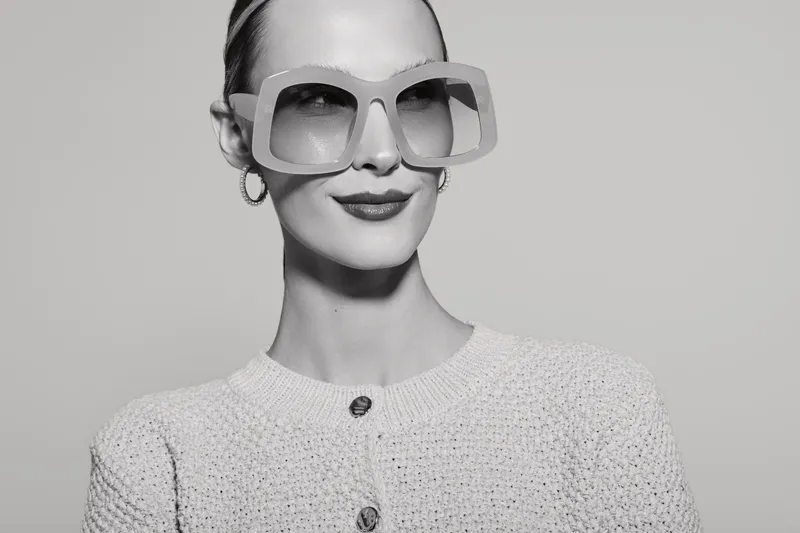 Stylish white woman with fair skin wearing large sunglasses and knitted cardigan against plain background. Concept of fashion, elegance, accessories, and confidence in studio.